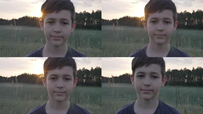 一个有趣的男孩在麦田里的肖像在日落时看着相机