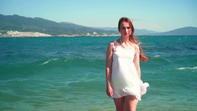 一个穿着白色沙滩装的女孩站在海边。一个光着脚的漂亮女孩站在海边。