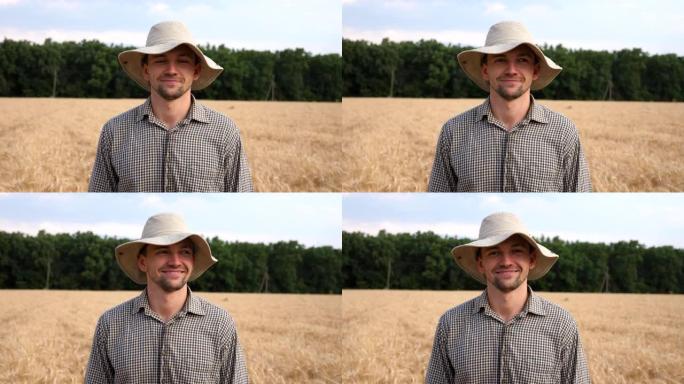 戴着帽子的快乐微笑的农民在麦田模糊的背景下看着相机的特写镜头。英俊的年轻农艺师站在大麦草地上的肖像。