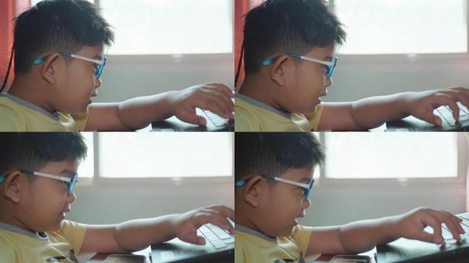 特写的快乐的亚洲儿童男孩戴着眼镜用笔记本电脑玩游戏，在一个房间里用智能手机看卡通，房间里有阳光从家里