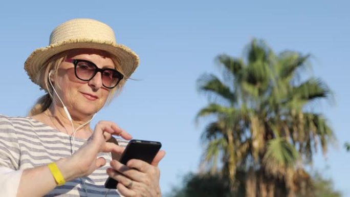 戴着墨镜和草帽的金发老妇在手机上选择一首歌。