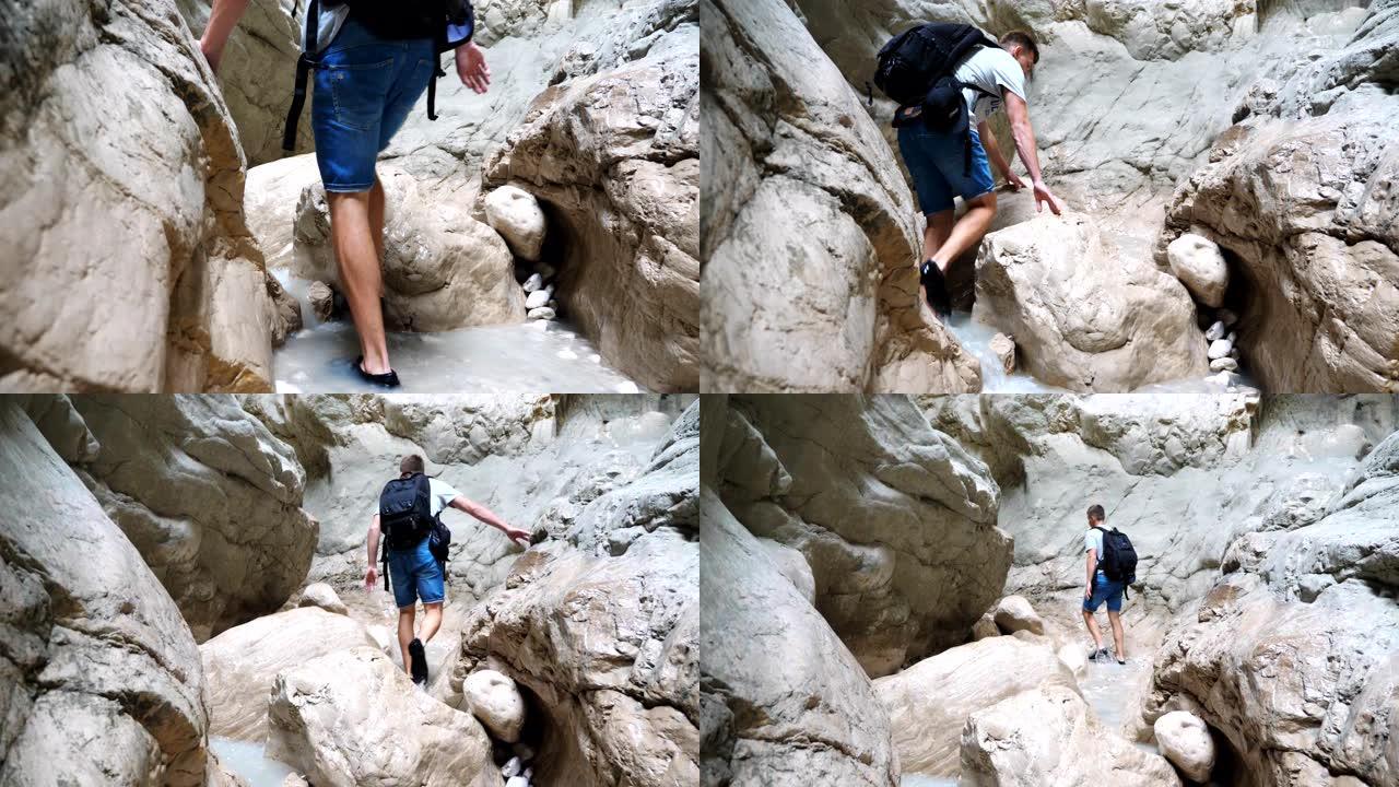 面目全非的年轻人背着背包走过狭窄的峡谷。探索岩石峡谷的男性徒步旅行者克服了困难的路线。旅行或主动休息