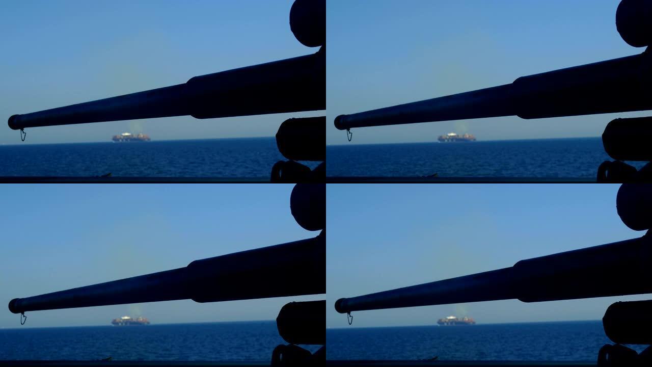战舰的炮管，背景是一艘货船