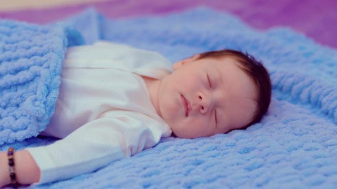 可爱的新生婴儿躺在床上，在被窝下睡得很香。肖像视图。