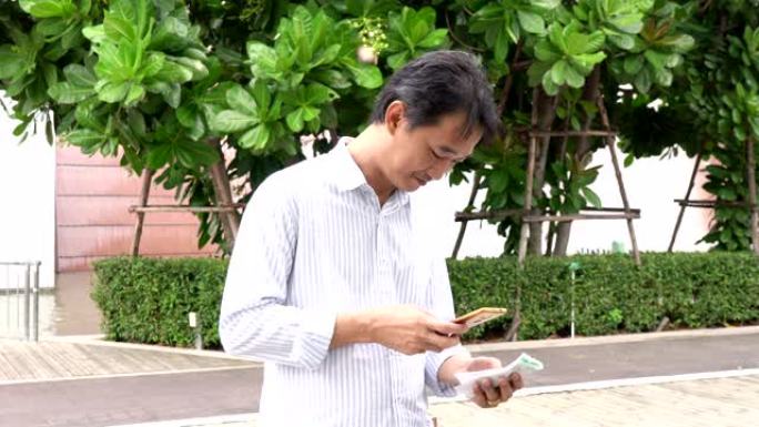 英俊的年轻商人拿着笔记本电脑，一边用手机站在街上