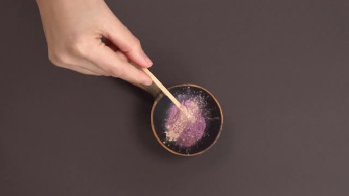 将草本紫粉放入木碗的俯视图。用手将白色干根粉加入碗中。生态产品制造