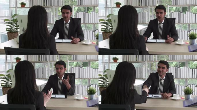 两个穿着黑色西装的商人男人和女人坐在办公室里聊天，在商务会议或求职面试协议商务上握手成交。