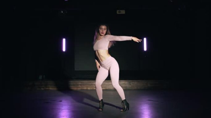 肖像美丽的女孩在粉红色紧身套装性感跳舞在黑暗的工作室与紫色的灯。编舞、舞蹈、表演的概念