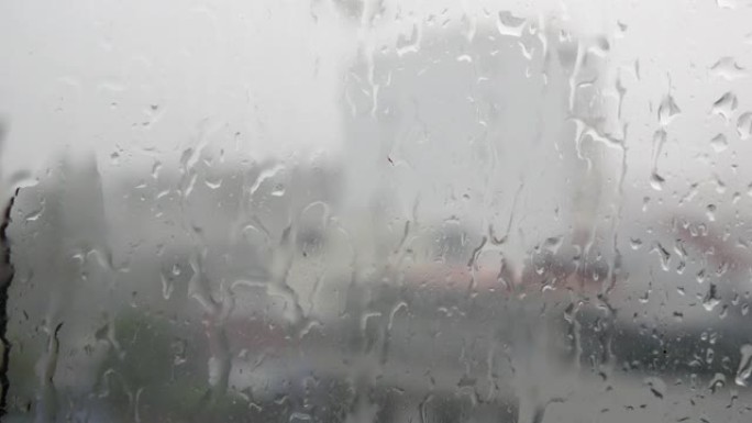 强烈的雨水冲向窗户玻璃并向下流动，关闭。雨季玻璃背景上的雨滴。4k