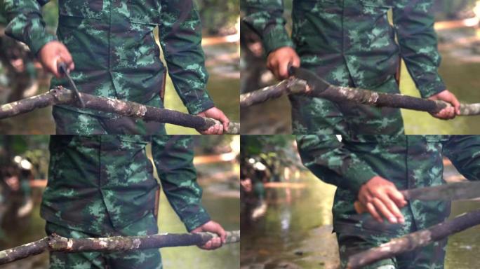 身着迷彩服的士兵用露营刀砍树枝在溪边的森林露营区生火的4K中拍。森林露营用柴火营火。