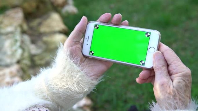 4k奶奶在花园里使用和看着绿屏智能手机