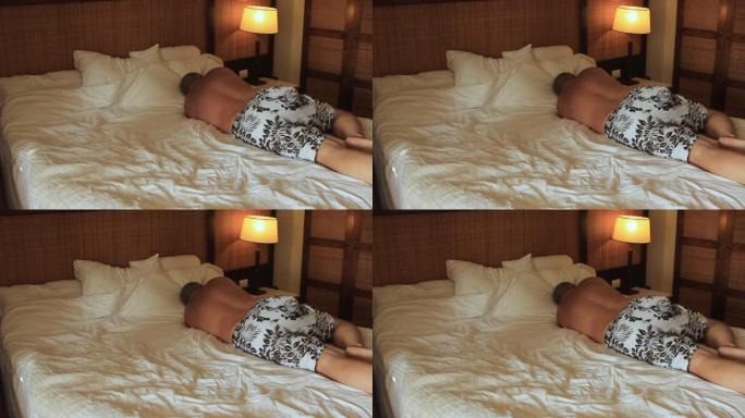 一个年轻人躺在旅馆的床上，躺在白色床单上，准备睡觉