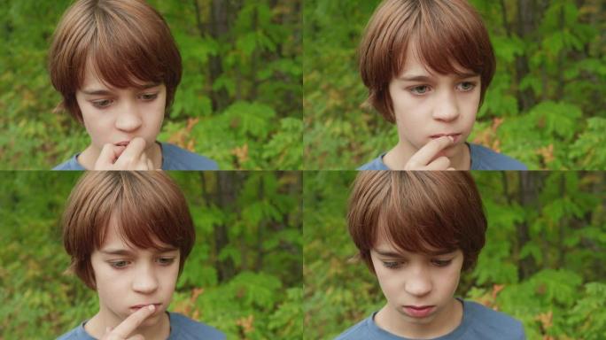 夏日公园的肖像思考少年男孩。英俊的少年男孩在户外嚼口香糖。绿树背景上小男孩沉思的脸。