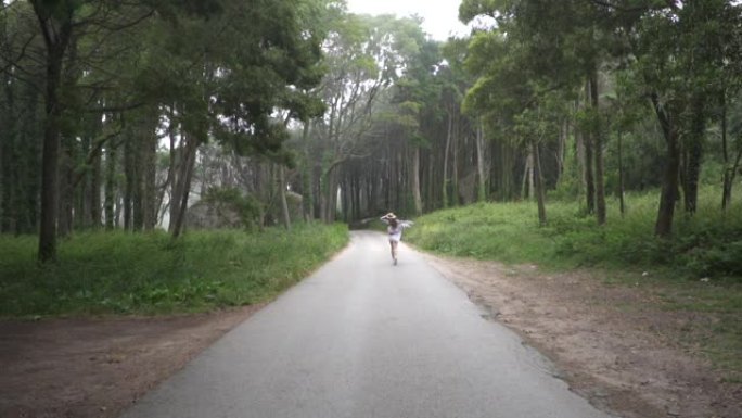 美丽的旅行者女孩穿着衣服和草帽走在柏油路上，在神奇的神话般的森林里，有高树和大石头。辛特拉。葡萄牙。