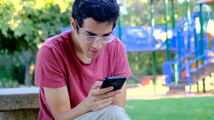 年轻人坐在公园的长凳上使用智能手机