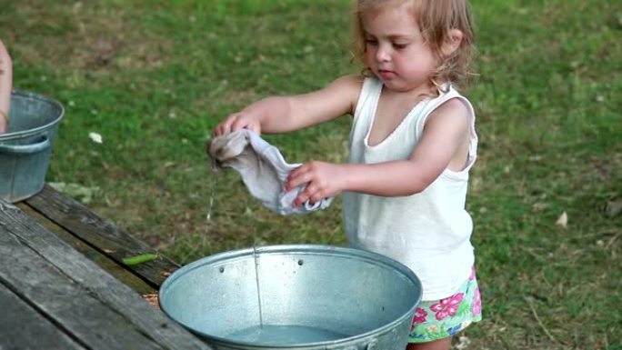 小女孩在金属盆里洗脏袜子