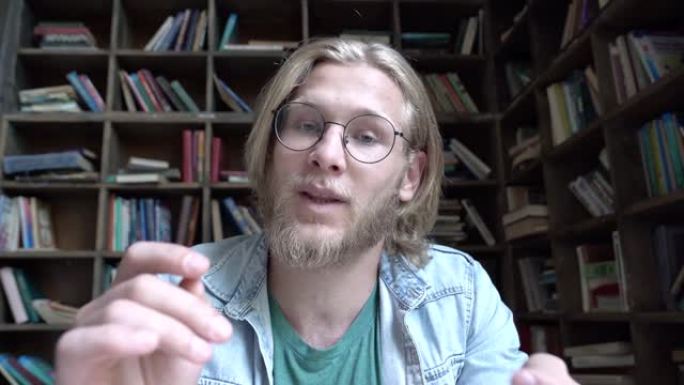 快乐的年轻人学生博客博客作者在图书馆里看着镜头说话拍摄教育vlog概念，现代男性影响者youtube