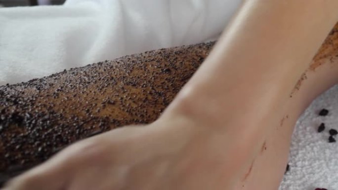 女按摩师的手在女人的腿上涂上咖啡磨砂面膜