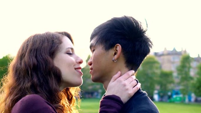 年轻的亚洲高加索夫妇在日落时在公园接吻和亲热，阳光照在后面