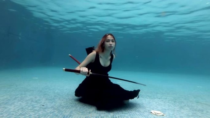 超现实女孩穿着黑色连衣裙，手里拿着一把红色武士刀，慢慢沉入水底。她拔出剑，展示它，然后玩弄它。肖像。