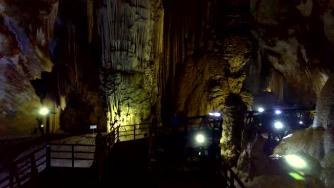 游客在洞穴中的灯线上漫步在黑暗的桥上