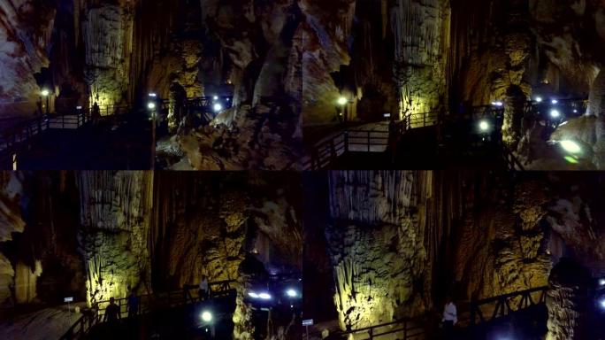 游客在洞穴中的灯线上漫步在黑暗的桥上