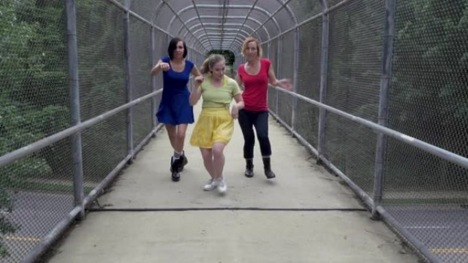 三个快乐的女人在有盖的人行天桥上向前跳舞