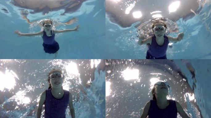 一个孩子，一个小女孩，正在从事水肺潜水。她戴着泳镜在游泳池水下游泳，看着相机微笑。特写。底视图。慢动