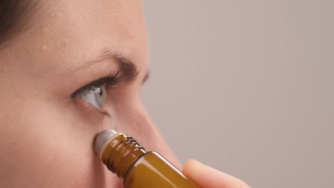 一名妇女使用滚装小瓶在面部皮肤上涂抹有机精油的特写镜头。天然护肤化妆品概念