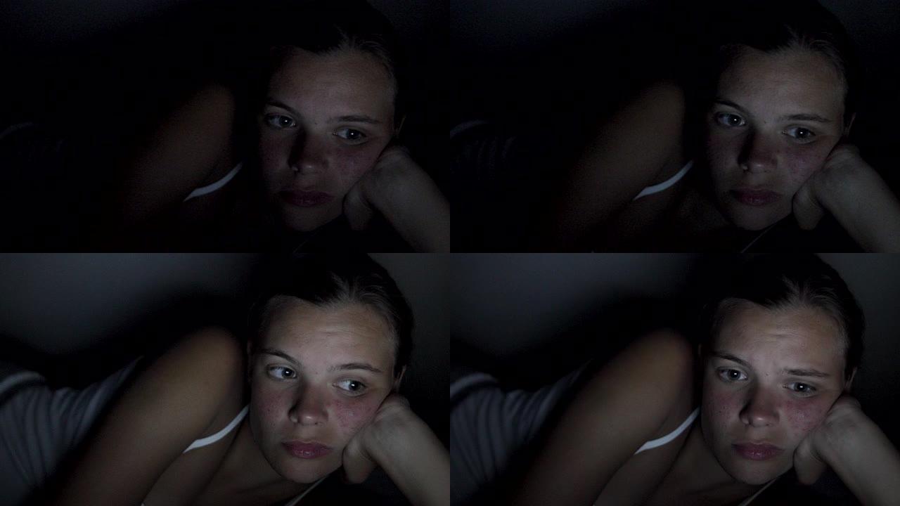 年轻的少女独自躺在床上，穿着睡衣看电影