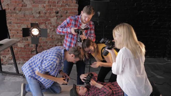 摄影后台，年轻摄影师用专业设备拍摄照片，戴着帽子的快乐女孩躺在桌子上，拿着相机