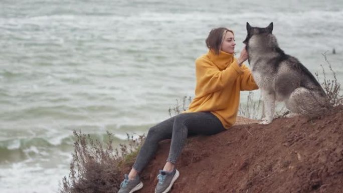 年轻漂亮的女性和西伯利亚哈士奇狗在海滩上散步。女人与哈士奇狗一起奔跑和玩耍