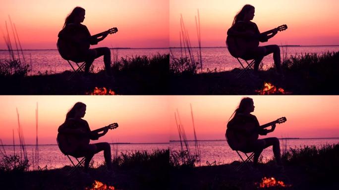 年轻女孩在日落时用篝火在海滩上弹吉他