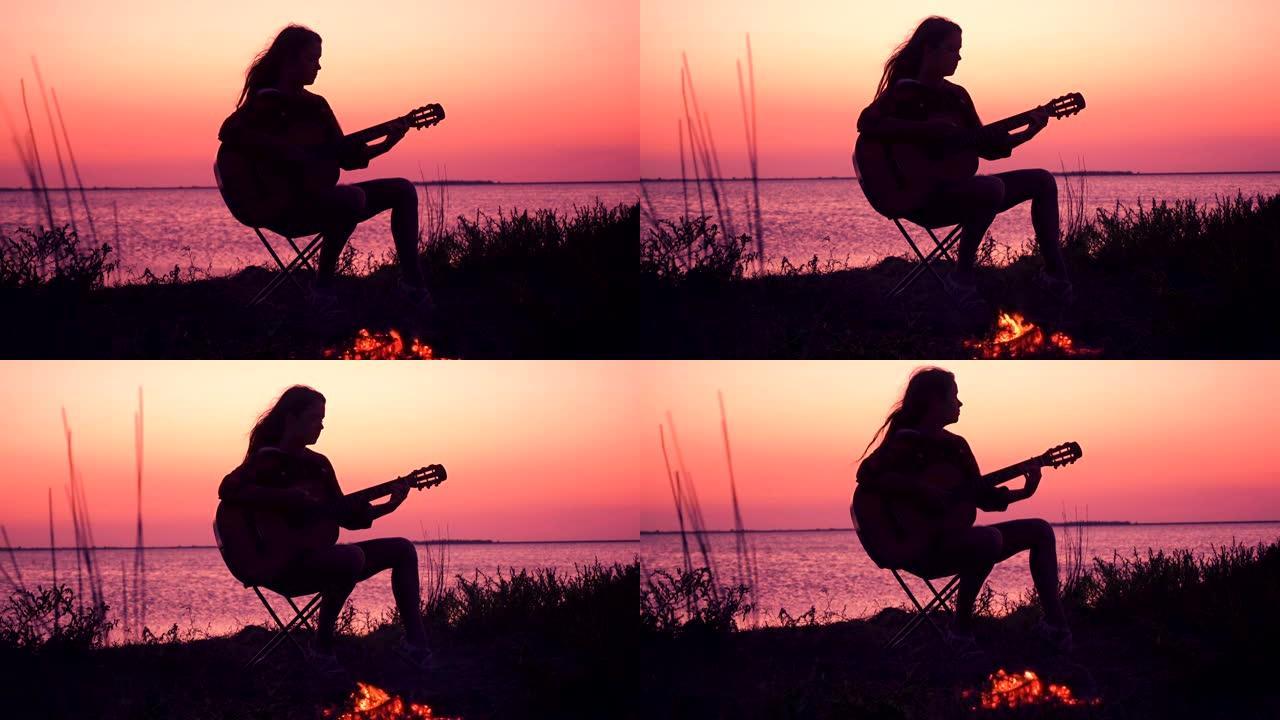 年轻女孩在日落时用篝火在海滩上弹吉他
