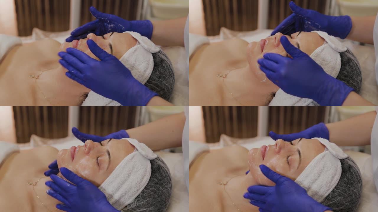 专业美容师用手按摩动作在女人脸上涂抹擦洗油