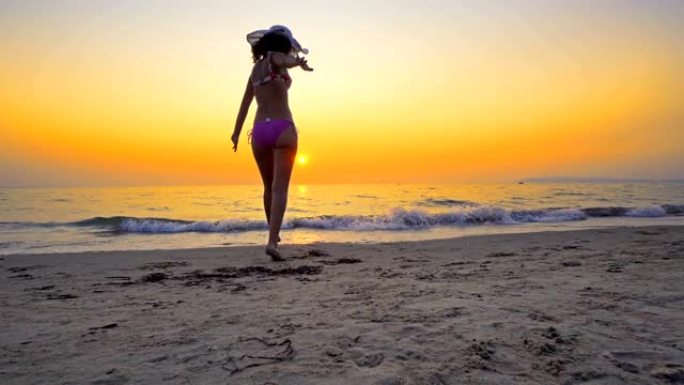 戴帽子的适合女性青少年在空旷的海滩上行走，双手张开，享受自由。女孩在日落时进入海水