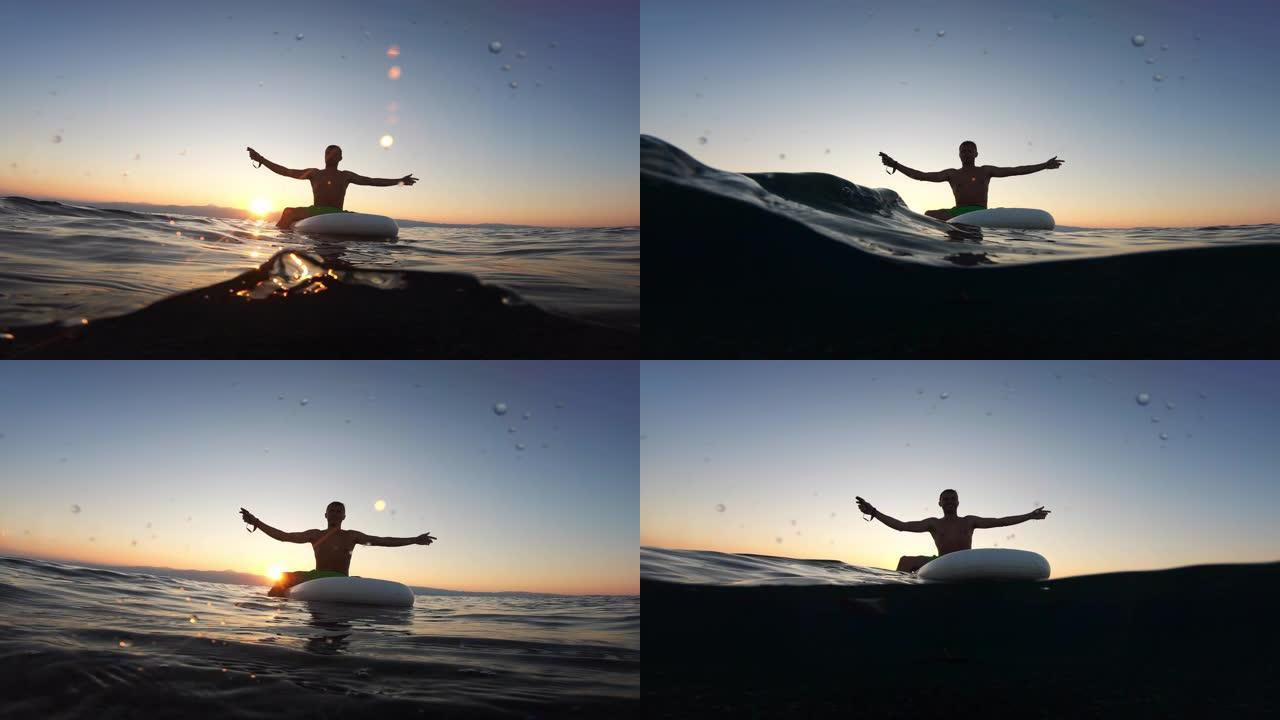 年轻的冲浪者坐在冲浪板上，在海上欣赏美丽的日落。冲浪是一种健身。躺在电动水翼冲浪板上的运动员。海洋中