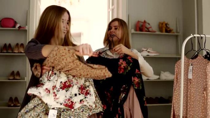 两个漂亮的女性，双胞胎姐妹在时装店拿着衣架和衣服，选择挂在架子上的衣服。前视图