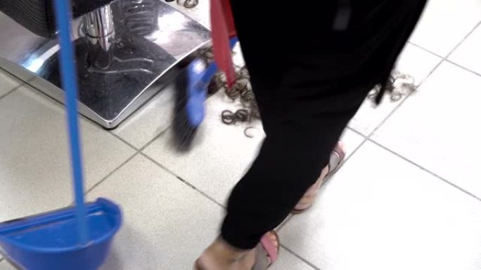 一名女清洁工在理发客户后，在理发店用扫帚在地板上扫头发。在理发店工作。从顶部看。特写。4K。