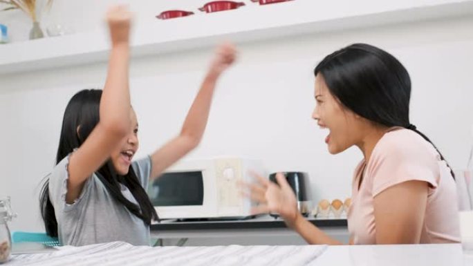 亚洲母亲的慢动作与女儿和女儿一起在家里的厨房里玩耍，以赢得胜利