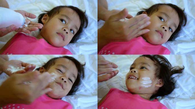 可爱的亚洲小女孩在妈妈洗澡后在床上涂滑石粉。护肤概念。