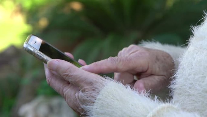 4k老奶奶的手拿着手机在花园的房子里