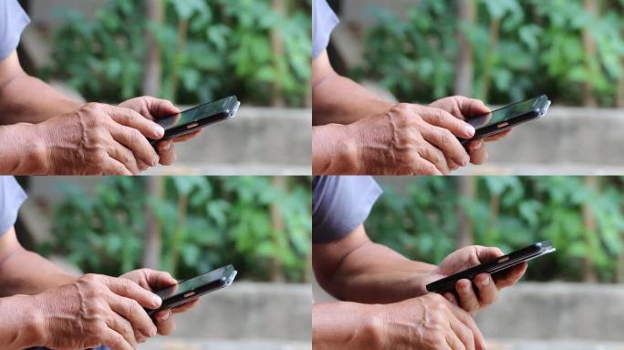 老人的手用左手拿着黑色智能手机，用右手手指触摸屏在花园里给家人发短信，家里有绿色的环境。在线，互联网