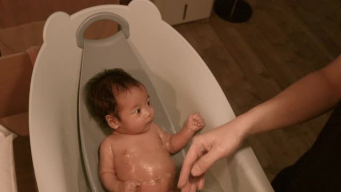 亚洲父亲给婴儿洗澡，婴儿躺在家里的浴缸里洗澡