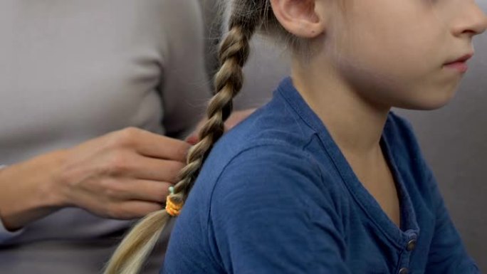 年轻的妈妈编织小女儿的头发，上学前的准备，特写