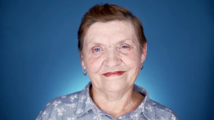 蓝色背景工作室微笑的老年妇女肖像。白人善良的祖母看着相机。