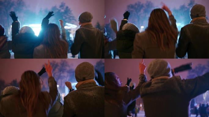 年轻人在城市广场的圣诞音乐会上聚会。朋友在新年市场音乐舞台上举手跳跃和双臂跳舞很有趣。冬季庆祝活动中