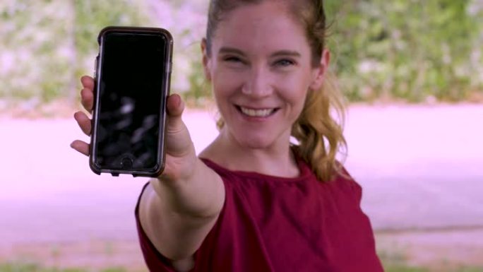 微笑的幸福女人展示她的手机显示屏并指着它