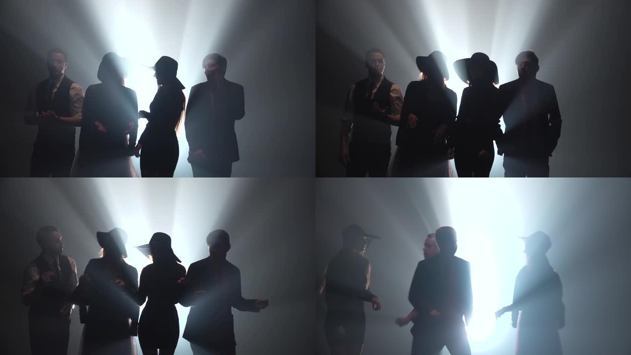 两个男孩和两个女孩站在黑暗工作室的聚光灯背景下，然后开始玩得开心，跳舞和唱歌。慢动作
