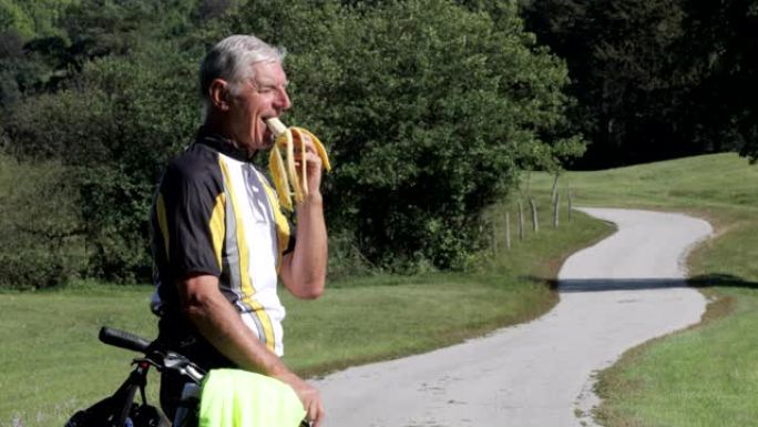 高级成人自行车手在乡下吃香蕉的侧视图